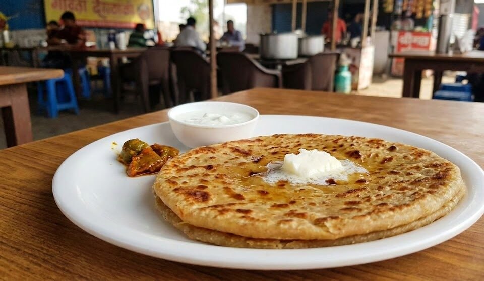 a plate of fresh paratha with white butter, curd, and pickle at a roadside dhaba, a popular stop on the delhi chandigarh route.