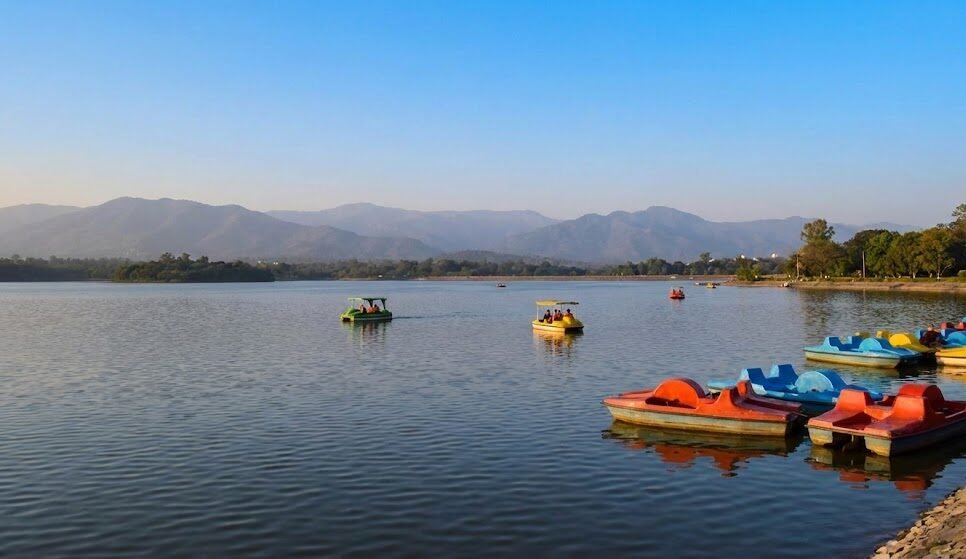 a scenic view of sukhna lake in chandigarh, with boats on the water and the shivalik hills in the background.