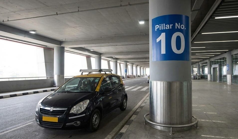 a taxi waiting at pillar no. 10 in the multi level car parking (mlcp) pickup zone at delhi airport terminal 3.